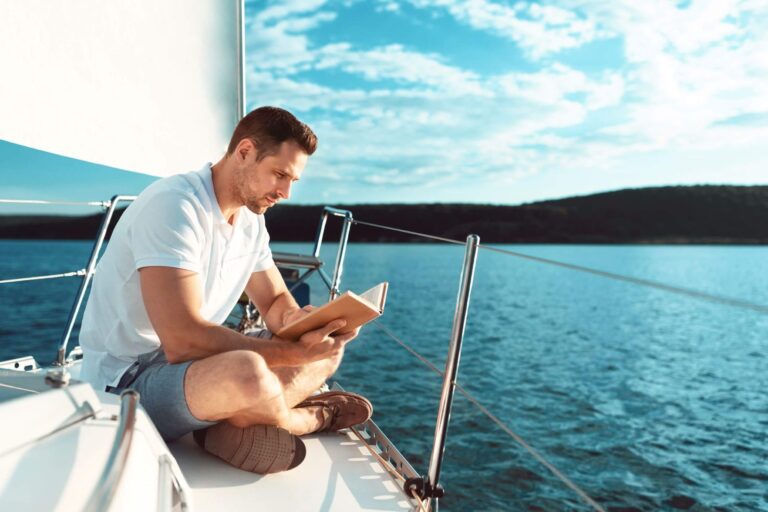 Man sitting on the bow of a sailing boat and reading